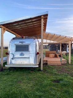 an old trailer is parked under a wooden awning in the middle of a field