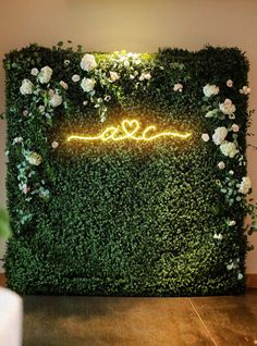 a green wall with white flowers and a neon sign that says love is in the air