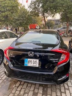 two cars parked next to each other on a brick road with trees in the background