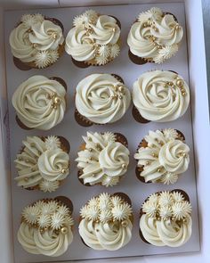 twelve cupcakes in a box with white frosting and gold decorations on them