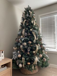 a christmas tree with gold and silver ornaments in a basket on the floor next to a window