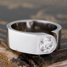 a white gold ring with a diamond in the center on top of a piece of wood