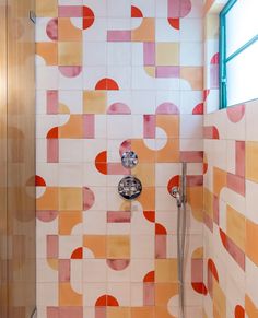 a tiled bathroom with orange and pink tiles on the wall, shower head and hand held faucet