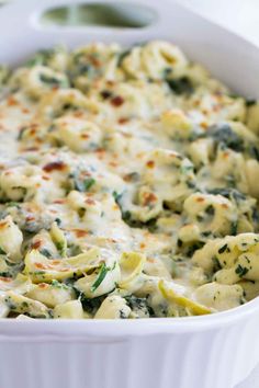 a white casserole dish filled with pasta and spinach covered in cheese sauce