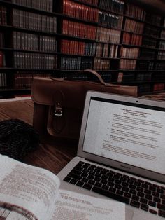 an open book sitting on top of a wooden table next to a laptop computer and bookshelves