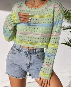 a woman wearing a green sweater and denim shorts with her hand on her hip, posing for the camera