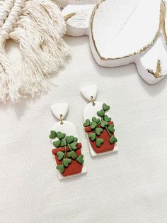 a pair of green and red earrings sitting on top of a white cloth covered table