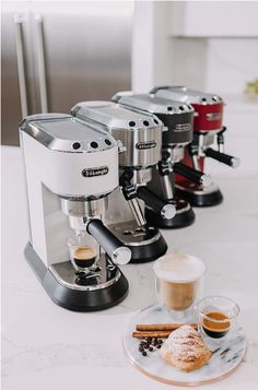 three espresso machines sitting on top of a counter next to coffee cups and pastries