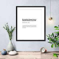 a white framed poster with the words tomorrow on it next to some potted plants