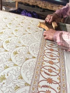 a man is working on an intricately designed table cloth with a wood block in his hand