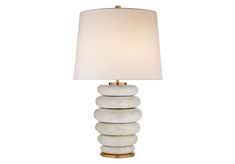 a white lamp with three stacked rocks on the bottom and a beige shade over it