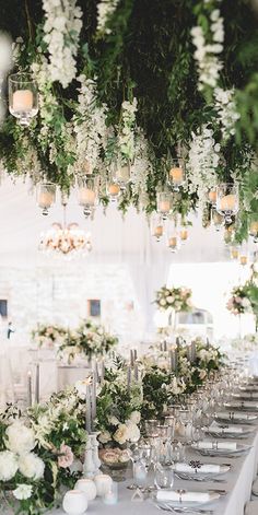 a long table with white flowers and greenery hanging from the ceiling is set for a wedding reception