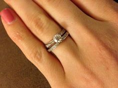 a woman's hand with two wedding rings on top of her finger and the other hand holding an engagement ring