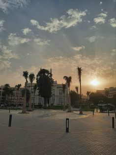 the sun is setting behind palm trees in front of a large white building with many windows