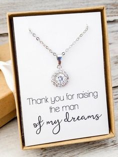 a card with a necklace in it on a wooden table next to a box that says thank you for raising the man of my dreams