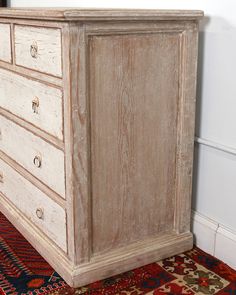 an old white dresser with drawers and knobs on the bottom drawer is sitting on a colorful rug