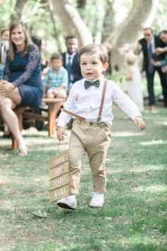 a little boy in a bow tie and suspenders walking down the aisle