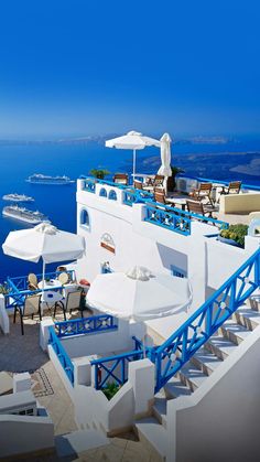 an outdoor dining area overlooking the ocean with blue and white tables, umbrellas and chairs