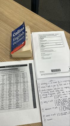 a stack of papers sitting on top of a wooden table next to a book and pen