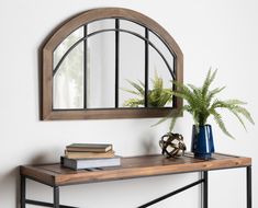 an arched mirror on a wall above a table with books and a potted plant