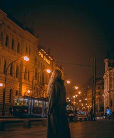 a woman standing in the middle of a street at night with her back to the camera