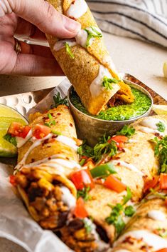 a person is taking a burrito out of a pan filled with salsa and guacamole