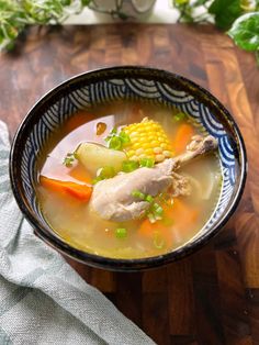 a bowl filled with soup and vegetables on top of a wooden table next to a napkin