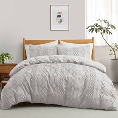 a bed with white comforter and pillows on it in front of a window next to a potted plant