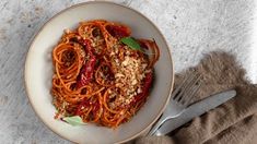 a white bowl filled with spaghetti and sauce on top of a table next to a fork