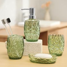 green glass bathroom accessories sitting on top of a wooden table