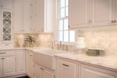 a kitchen with white cabinets and marble counter tops