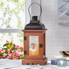 a lantern with a photo on it sitting next to some books and flowers in front of a window