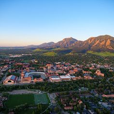 an aerial view of a city with mountains in the back ground and grass on the other side