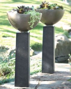 three metal vases with plants in them sitting on the ground next to some rocks