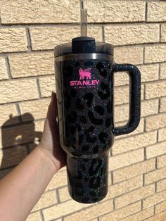 a person holding up a black and pink coffee mug with glitter on it's side