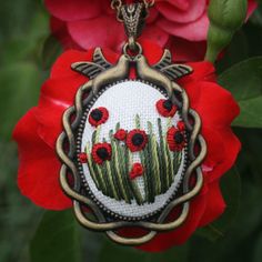 a cross stitch necklace with red flowers in the center and green grass on the bottom