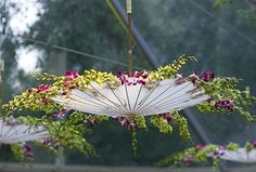 an umbrella with flowers hanging from it's side in front of some trees and bushes