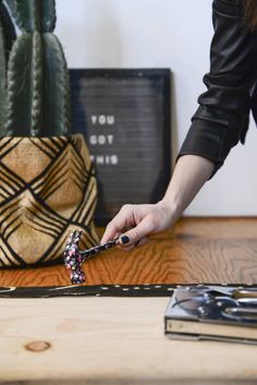 a woman is using scissors to cut fabric on a table next to cacti