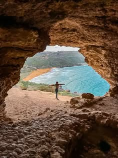 a person standing in the middle of a cave looking out at the water and land