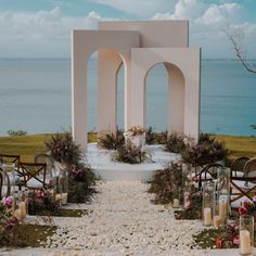 an outdoor ceremony setup with candles and flowers on the ground next to the water in front of it