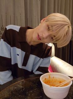 a young boy sitting at a table with a bowl of food in front of him