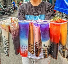 a man holding up four cups with different colored drinks in them on top of each other