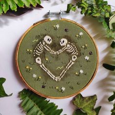 two skeletons in love cross stitched together on a green background surrounded by greenery