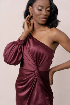 a woman in a maroon dress is holding her hand on her shoulder and looking down