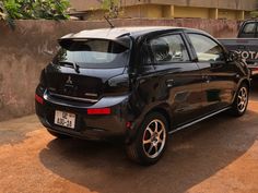 a small black car parked in front of a cement wall with another vehicle behind it