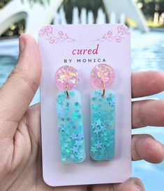 a pair of blue and pink earrings with stars on them in front of a pool