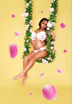 a pregnant woman laying on top of a lush green plant covered in pink and white flowers