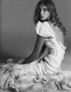 a woman sitting on top of a bed in a white dress