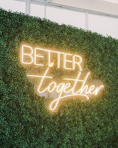 a sign that says better together on top of a green wall with bushes behind it