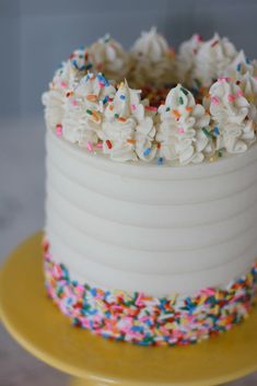 a white cake with sprinkles on top sitting on a yellow platter